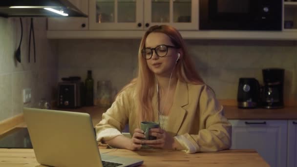 笔记本电脑后面的女人在家里工作 一个穿着夹克和眼镜的金发美女通过视频通话 老师在网上授课 自由职业教师 — 图库视频影像