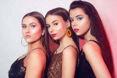 Beyaz arka planda üç güzel esmerin portreleri. Kızlar 8 Mart Kadınlar Günü 'nü kutluyor. Güzel kadınlara makyaj, aksesuarlar ve parıltılı kıyafetler.