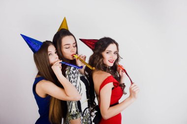 Zarif bir gece elbisesi içinde kutlama yapan, eğlenen, beyaz arka planda dans eden üç güzel kadının çılgın parti zamanı. Pembe arka planda parti şapkalı kızlar.. 
