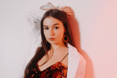 Parlak kırmızı elbiseli muhteşem bir esmer dans ediyor, beyaz ceketli bir model eğleniyor. Sarı aksesuarlı, küpeli ve pembe makyajlı bir kız..