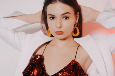 Parlak kırmızı elbiseli muhteşem bir esmer dans ediyor, beyaz ceketli bir model eğleniyor. Sarı aksesuarlı, küpeli ve pembe makyajlı bir kız..