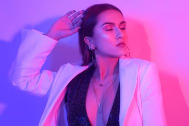 Büyük dudakları, mükemmel kaşları, büyük küpeleri ve pirzolaları olan muhteşem bir esmerin portresi. Neon ışıklı şık bir kız. Bir parti. Beyaz ceketli kız..