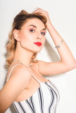 Stüdyoda beyaz arka plandaki kız çizgili tulumla dans ediyor. Kıvırcık saçlı ve dudaklarında kırmızı ruj olan güzel sarışın kadın. Yeni pim biçimi