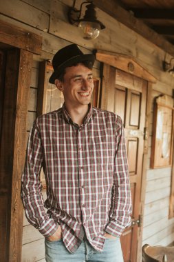 Erkek kovboy evinin yakınında. Western, kovboy şapkalı adam gülümsüyor. Erkek batı şehri. Turizm, geceyi geçirmek için ilginç yerler.