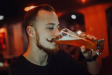 Barda bira içen bir adam, barda uzun bıyıklı, kızıl saçlı yakışıklı bir adam..