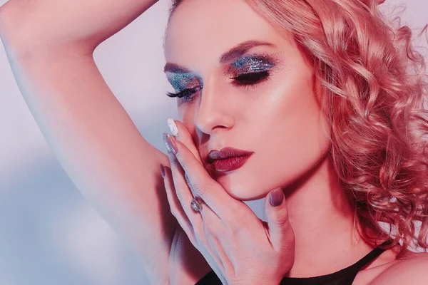 Blonde in silver and diamonds, obesity, earrings, rings. Woman with beautiful long nails and manicure. Girl with shiny makeup in neon. Glitter makeup, red lips
