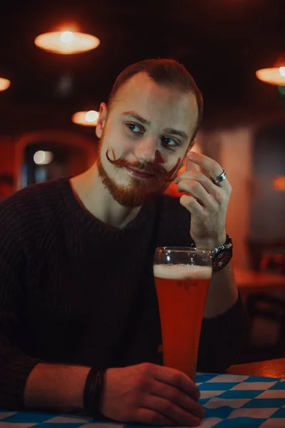 A man in a bar drinks beer, a handsome red-haired guy with a long mustache in a pub.