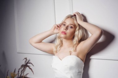 Balodaki beyaz elbiseli güzel sarışın. Gelinlik giymiş gelin. Narin makyajlı, saç stili ve gümüş küpeli bir kızın portresi..