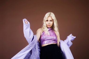 Mor ceketli, kahverengi arka planda 70 'li, 80' li yaşlarda 90 'lı yaşlarda, uzun gümüş küpeli bir kız. Sarışın dans ediyor, poz veriyor, moda yapıyor. Yakışıklı bir kadın..