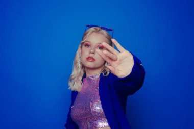 Mavi arka planda, 70 'li, 80' li, 90 'lı yıllarda makyajlı mavi ceketli bir kız yüzünü bir yıldız gibi eliyle kapatıyor. Parlak ceketli bir kız..