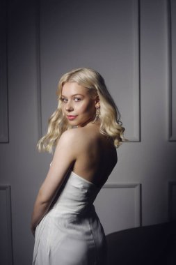 Beyaz gelinlik giymiş güzel bir sarışın. Makyajlı, şekilli ve gümüş küpeli bir kadın. Gelin çok güzel. Model kameraya bakıyor..