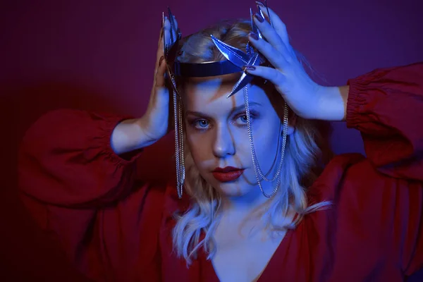 Portrait in neon of a woman in a silver crown with chains. The girl in the role of the princess. Fashion shooting a portrait in red and blue neon. Beautiful model wears a crown with an angry face, confidence. Coronation.