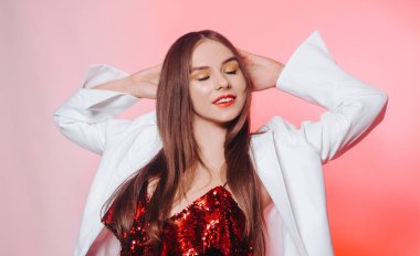 Parlak kırmızı elbiseli muhteşem bir esmer dans ediyor, beyaz ceketli bir model eğleniyor. Sarı aksesuarlı, küpeli ve pembe makyajlı bir kız..