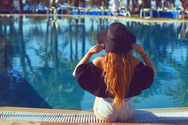 Siyah şapkalı, kırmızı dudaklı, havuz başı avuçlarında poz veren güzel bir kız. Güzel kız yanar, dinlenir, dinlenir, seyahat eder..