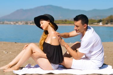 Yaz tatilinde olan güneş kremi çifti yüksek güneş kremiyle cilt bakımı yapar. Güneş kremi süren bir çift. Yakışıklı adam kumsalda kız arkadaşına güneş kremi sürüyor.. 