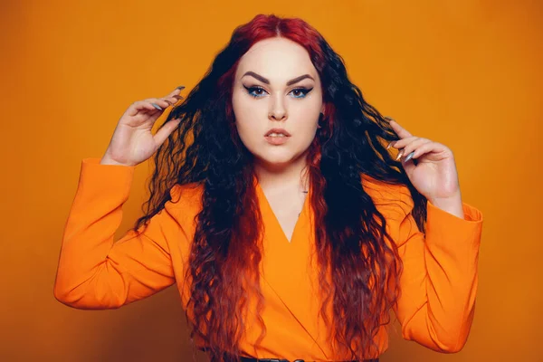 A woman with red roots and black hair. Unusual hairstyle, hairdresser, wind in your hair. Girl on a yellow background in an orange dress. Fashion and beauty.