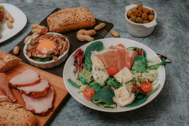 Et, ekmek ve aperatiflerle dolu bir şölen masası. Çırpılmış yumurta, jambon, zeytin ve vejetaryen pirzolası. Öğle yemeği mi akşam yemeği mi? Harika bir kahvaltı. Salata ve peynir..