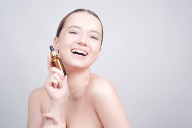 Güzel esmer bayanın yüzüne pipetle kozmetik yağ sürdüğü yakın plan. Güzellik terapisi konsepti. Temiz cilt ve yüz bakımı. Gençlik ve kozmetik gülümsemesi esmer