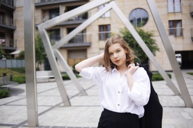 Öğrenci, menajer, emlakçı, binanın arka planında poz veren beyaz gömlekli kız. Kısa saçlı güzel bir sarışın. Kırmızı dudaklı ve siyah ceketli bir model..