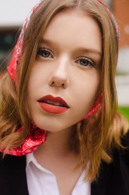 İnanılmaz güzel mavi gözlü bir kızın portresi. Modaya uygun bir fotoğraf. Kıyafet modası, ipek fularlı bir kız, kırmızı ruj ve mavi gözler. Kısa saçlı sarışın.
