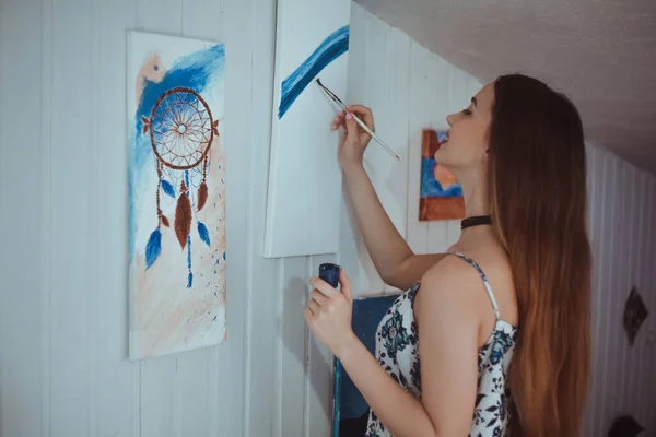 Cute girl painting a picture in home studio. Beauty model woman painting her picture. Art. Woman draws paints. Sweet girl engaged in creativity. Model painting brush on easel. Young artist painting .