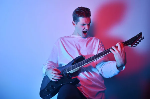 Portrait of young man artist singing, screaming, playing electric guitar Hobby, music concept. Rock Star The guy in neon plays the guitar and sings. Music