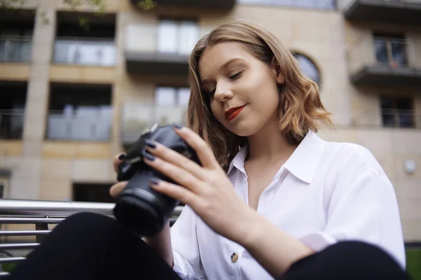 カメラのファインダーを覗くと美しい少女が写真を撮っている ブロンドは写真を学び 写真でお金を稼ぐことを学びます 少女写真家が街を歩き写真を撮る — ストック写真