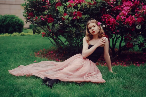 Dívka Dlouhých Růžových Šatech Sedí Zahradě Trávě Pozadí Růžových Květin — Stock fotografie