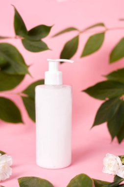 Kozmetik, krem ve şeker, pembe arka planda losyon. Yaprak ve çiçeklerden oluşan beyaz bir şişe. Doğal Kozmetik