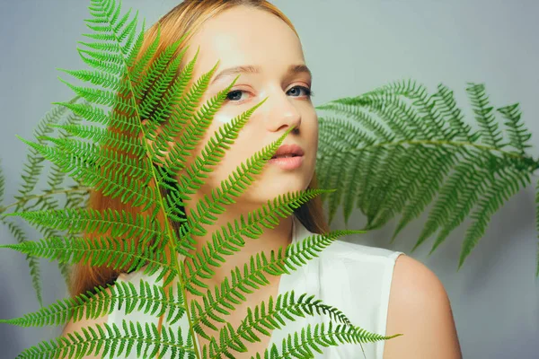 Beautiful young blond woman with perfect skin and natural make up posing front of plant tropical green leaves background. Teen model hair care of her face Fashion.