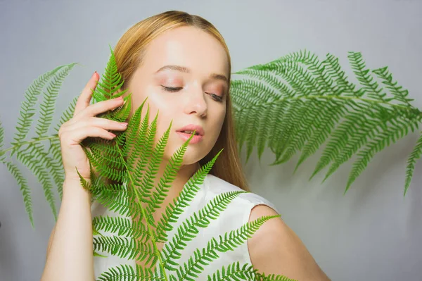 美丽的金发女子有着完美的皮肤和自然的妆容 构成了植物热带绿叶的背景 青少年模特儿的面部护理 — 图库照片