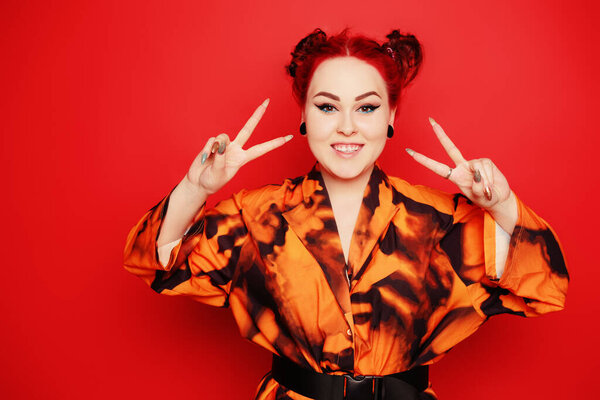 Cute girl on a red background. Red hair and tunnels in the ears, red dress and lips. Anime poses. The girl with eyeliner and two buns on her head grimaces, smiles, has fun. Japanese culture