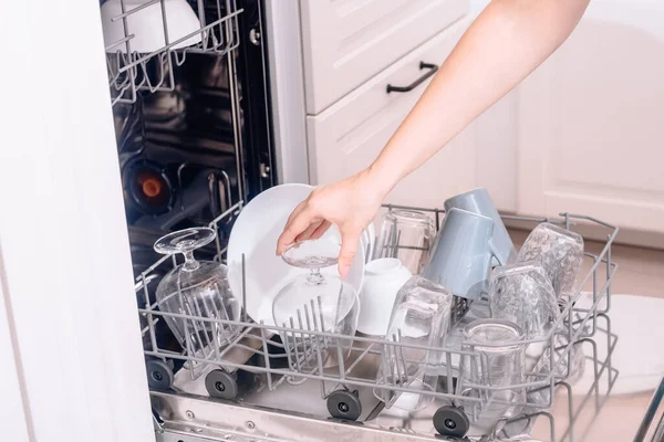 Built-in dishwasher, dishwashing. A woman loads washed dishes, cups, glasses. A woman\'s gentle hand puts something in the dishwasher or pulls out, unloads.