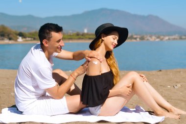 Yaz tatilinde olan güneş kremi çifti yüksek güneş kremiyle cilt bakımı yapar. Güneş kremi süren bir çift. Yakışıklı adam kumsalda kız arkadaşına güneş kremi sürüyor.. 