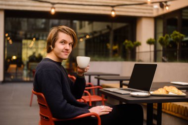Terasta bir restoranda kahve içen bir adam. Dışarıda dizüstü bilgisayarı olan serbest çalışan, kruvasanlarla kahvaltı yapan biri. İş adamı görünüşü ve hayalleri. Dizüstü bilgisayarlı adam