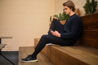 Bir öğrenci portresi bankta oturur ve telefona bakar. Bir adam ekrana bakar ve SMS yazar, güzel hava. Kazaklı adam.