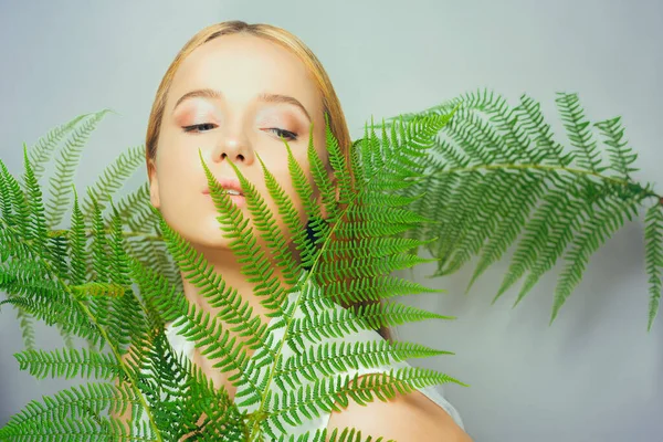 Beautiful young blond woman with perfect skin and natural make up posing front of plant tropical green leaves background. Teen model hair care of her face Fashion.