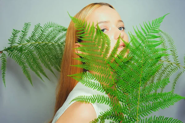 Beautiful young blond woman with perfect skin and natural make up posing front of plant tropical green leaves background. Teen model hair care of her face Fashion.