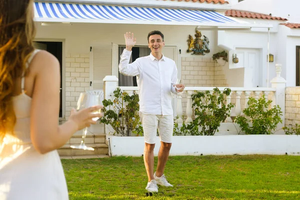 Couple celebrating buying a house by the ocean. couple drinks wine near the house. Couple rejoices, smiles, laughs. Beautiful girl in a white dress on a date with a man in white. Romantic travel.