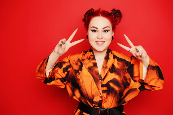 Cute girl on a red background. Red hair and tunnels in the ears, red dress and lips. Anime poses. The girl with eyeliner and two buns on her head grimaces, smiles, has fun. Japanese culture