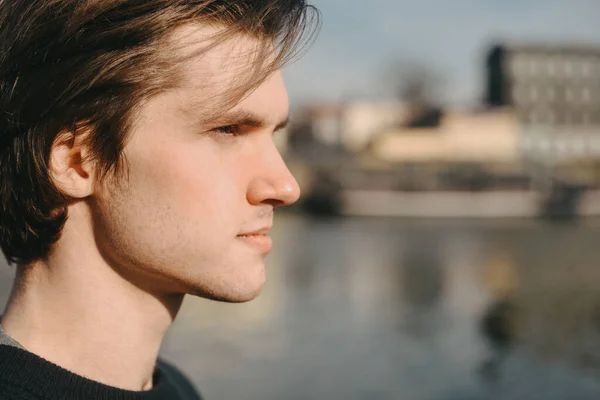 Profile of a man on a sunny day. The guy on the background of the river in Europe looks into the distance. Portrait of a guy