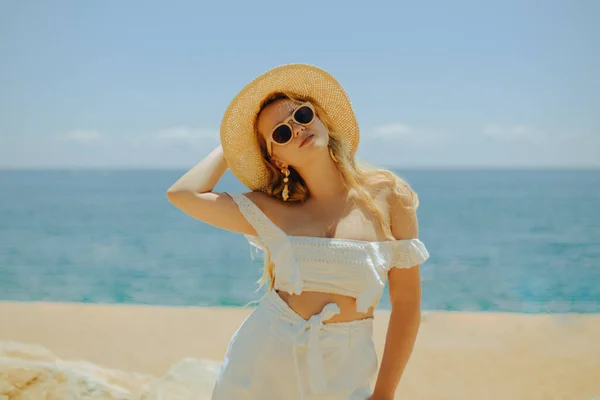 美丽的女孩在海滩 大海和大海的背景下 一个穿着白色衣服 戴着太阳镜 头戴大帽子的金发女郎正在度假 享受夏天的假期 — 图库照片