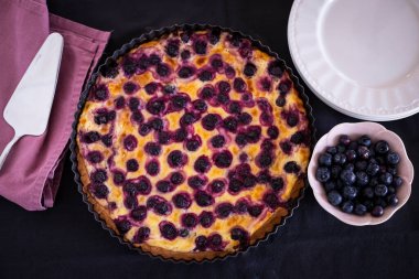 Mustikkapiirakka, bir Fin yabanmersinli turtası. Düz yatıyordu, mavi elbisenin üstünde beyaz tabaklar ve bir kase taze meyve vardı..