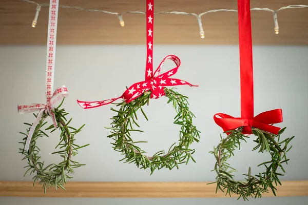 Kırmızı kurdelelerle süslenmiş üç biberiye çelengi bir rafta asılı. Doğal ev dekorasyonu, diy, Noel için fikir.