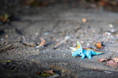 Minyatür dinozor oyuncağı, mavi triceratops, doğal ortamında yerde yürüyor. Kopyalama alanı olan arkaplan.