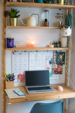 Küçük ofis uzaktan kumandası, çalışma alanı, dizüstü bilgisayarı, ev bitkileri, duvar tahtası ve mumları. Dikey çekim.