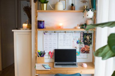 Küçük ofis uzaktan kumanda istasyonu, çalışma alanı, dizüstü bilgisayarı, ev bitkileri, duvar tahtası ve mumları olan..