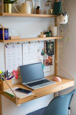 Küçük ofis uzaktan kumandası, çalışma alanı, dizüstü bilgisayarı, ev bitkileri, duvar tahtası ve mumları. Dikey çekim.