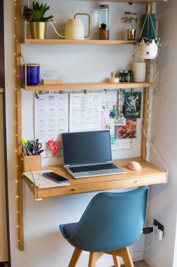 Küçük ofis uzaktan kumandası, çalışma alanı, dizüstü bilgisayarı, ev bitkileri, duvar tahtası ve mumları. Dikey çekim.