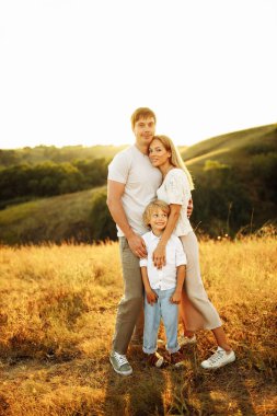 Okul öncesi çocuğu olan güzel ebeveynler sahada yürüyorlar, kocalarını seviyorlar sevimli eşlerine sarılıyorlar, mutlu bir aile birlikte vakit geçiriyorlar, çocukluk ve ebeveynlik kavramının tadını çıkarıyorlar.